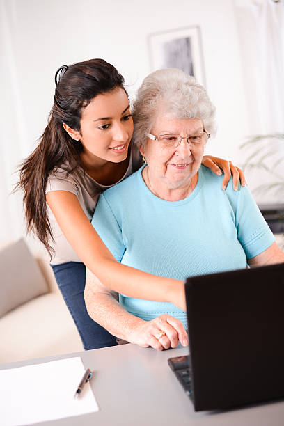 istock cheerful young woman teaching computer and internet to elderly person 509488997