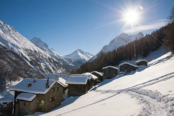 Swiss Alpine village in the snow with sun star and flare.