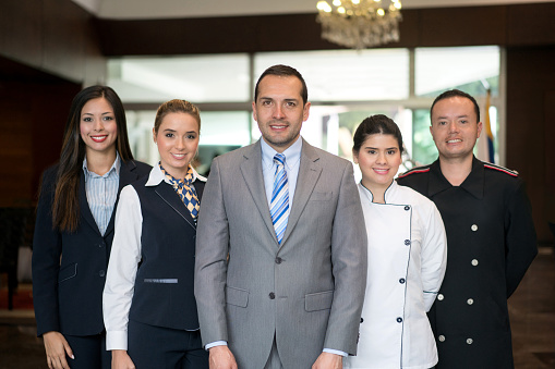 Portrait of hotel staff group including manager, receptionist, chef and bellboy looking at the camera smiling