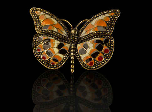Coloured enamel brooch butterfly isolated on black with reflection.