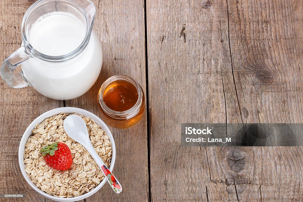 Healthy cereal with milk, honey and strawberry Healthy oatmeal with milk, honey and strawberry on wooden table Agriculture Stock Photo