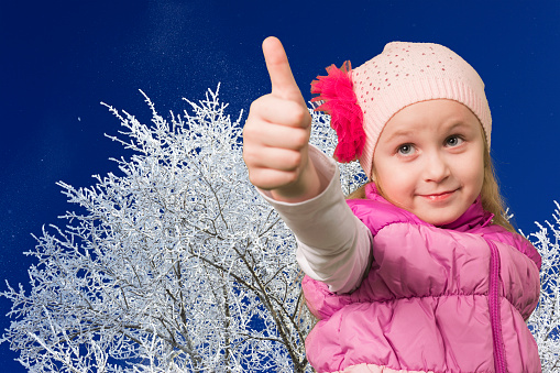 Cute little girl showing ok on winter background