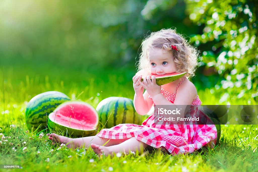 Little girl eating watermelon Child eating watermelon in the garden. Kids eat fruit outdoors. Healthy snack for children. Little girl playing in the garden holding a slice of water melon. Kid gardening. Watermelon Stock Photo