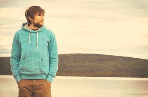 Young Man hipster standing alone outdoor with mountains and lake on background Lifestyle and melancholy emotions concept