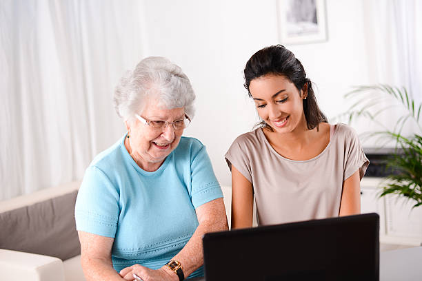 istock cheerful young woman teaching computer and internet to elderly person 509514721