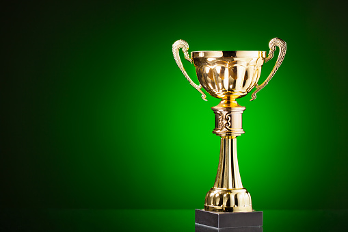 gold cup trophy on green background with copy-space