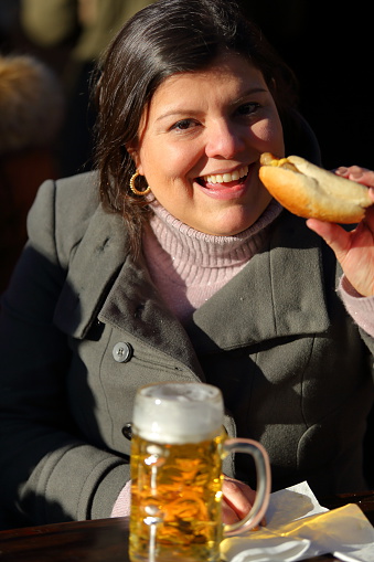 Lady enjoying hot dog and beer during a visit to the Munich beergarden at viktualienmarkt. Typical food and drink of the counrty.