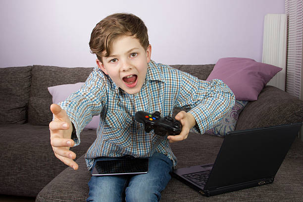 Young boy playing on tablet, game console and laptop stock photo