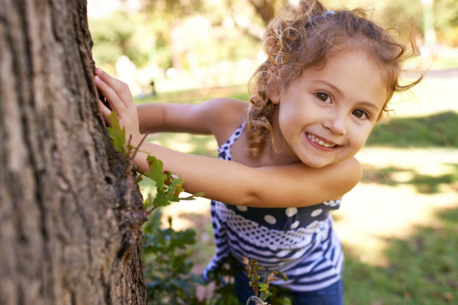 Portrait of a little girl hiding behind a tree in a park