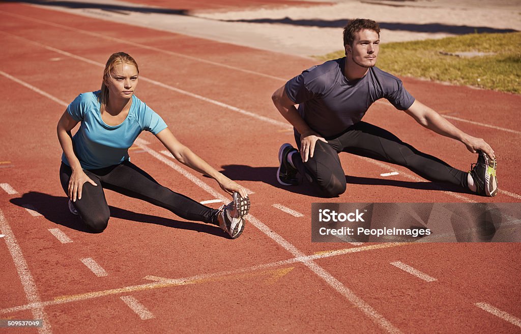 Warming up to take you down Shot of two young people stretching on an athletics track 20-29 Years Stock Photo