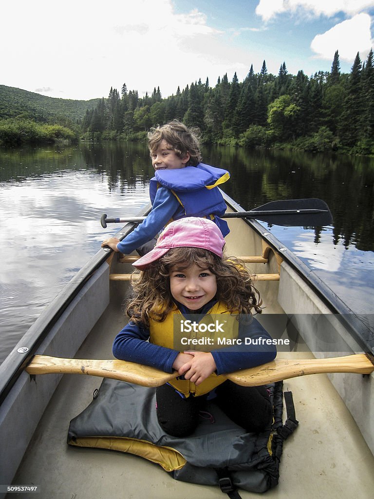 Go Daddy Two little kids in a canoe are looking at their dad paddling behind 4-5 Years Stock Photo