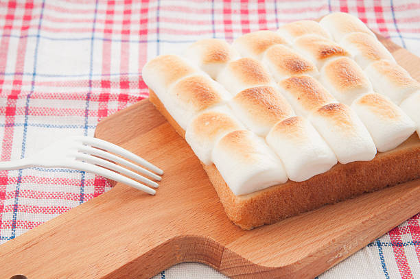 Fingers holding  toast with bites out of it, yeast spread.