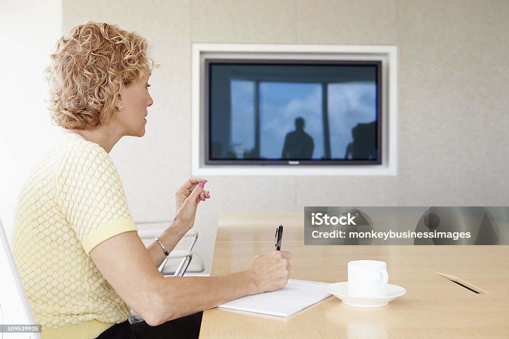 Senior Businesswoman Having Video Conference In Boardroom Senior Businesswoman Having Video Conference In Boardroom Sitting At Table Holding Pen Meeting Room Stock Photo