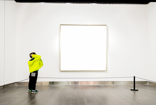 Asian boy looking at white frames in an art gallery.