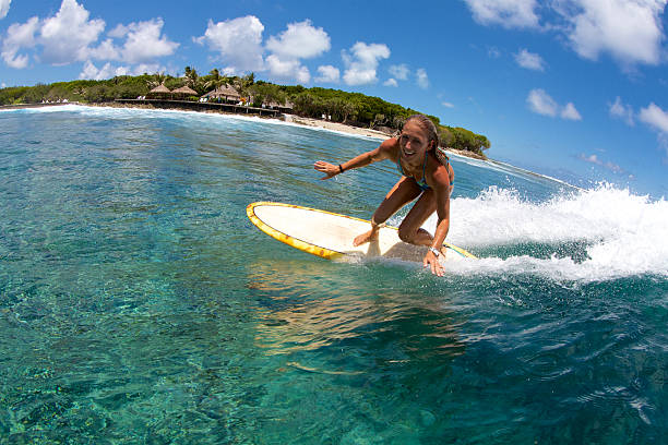 A girl smiles with delight as she bottom turns on a single fin surfboard in perfect blue water.