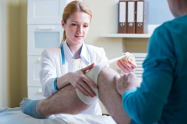 Nurse rewinding knee bandage Female doctor is rewinding knee bandage to man. Doctor taking care of a patient with trauma of patella human spine photos stock pictures, royalty-free photos & images