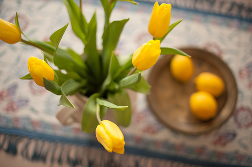 Yellow tulips in vase  and metal bow with fresh lemons from above on a table with tablecloth. Horizontal shoot. 