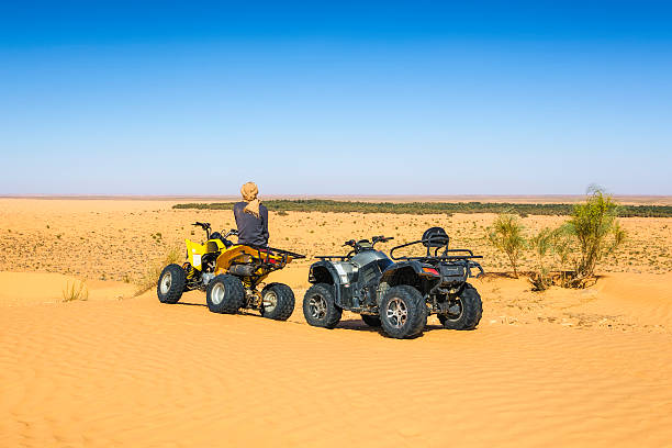 Quad Trip in Sahara desert near Ksar Ghilane oasis , Tunisia Ksar Ghilane, Tunisia - April 14, 2015: Tuareg sitting on a quad bike, view to the oasis of Ksar Ghilane. Quad bike tour in the Sahara desert Grand Erg Oriental / Great Eastern Sand Sea in Tunisia. trailblazing stock pictures, royalty-free photos & images