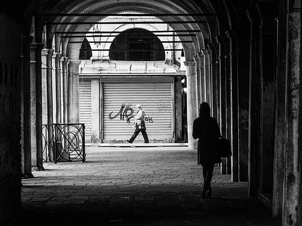 Venice, Italy - October 14, 2013: Monochrome image of a woman waiting under an archway as a man walks past.  Contemporary street scenes of Venice, Italy