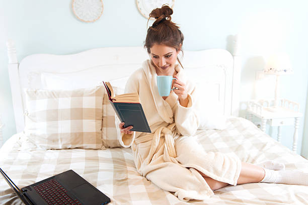 istock Young woman sitting on the bed, reading a book 509555026