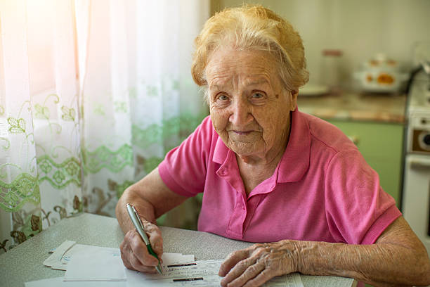 une femme âgée emplit la facture sur les factures de services publics. - women poverty senior adult mature adult photos et images de collection