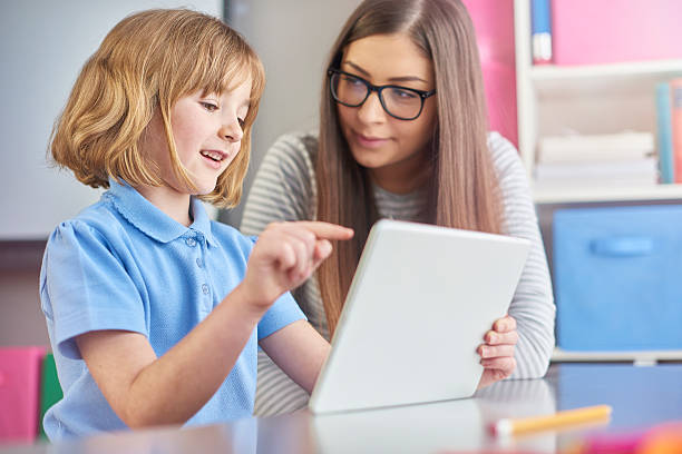 good teachers know when to listen a young teacher listens as her young pupil explains what she is reading on a digital tablet . The little girl is excited as she explains to her teacher . elementary student pointing stock pictures, royalty-free photos & images