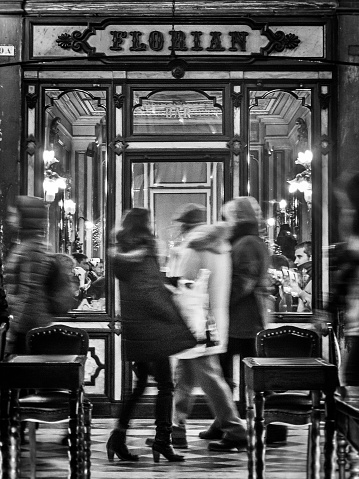 Venice, Italy - November 29, 2013: Monochrome image of a woman walking past the Florian Caffe in St Mark's Square.  Contemporary street scenes of Venice, Italy