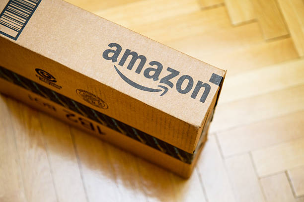 Amazon logotype printed on cardboard box Paris, France - January 28, 2016: Amazon logotype printed on cardboard box side seen from above on a wooden parwuet floor. Amazon is an American electronic e-commerce company distribution worlwide e-commerce goods amazon stock pictures, royalty-free photos & images