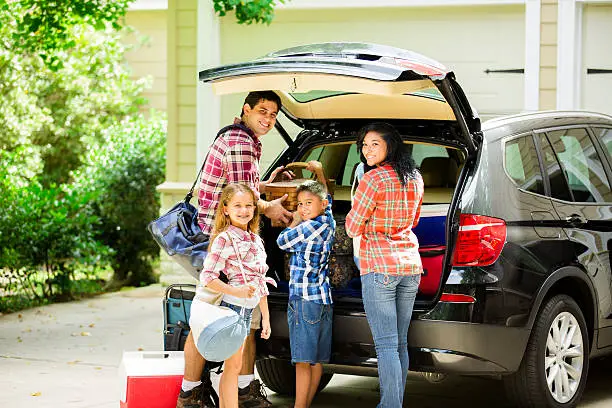 Mother, father and their two children pack the family car to go on vacation.