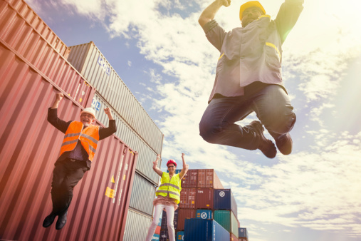three workers in a large container port, jumping for joy