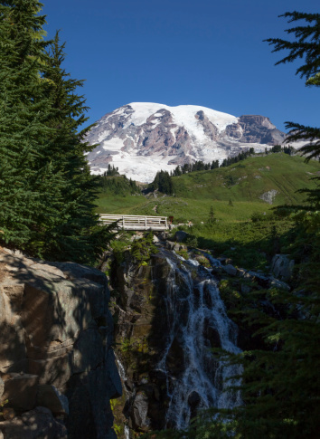 This image shows Myrtle Falls cascading down over the rocks with Mount Rainier in the background on a sunny summer morning.