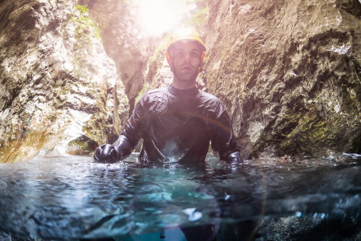 Male canyoning team member walking in the water pool in the canyon.