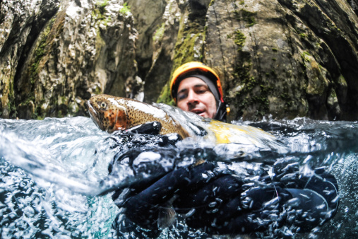 Male canyoning team member in the water pool holding a trout.