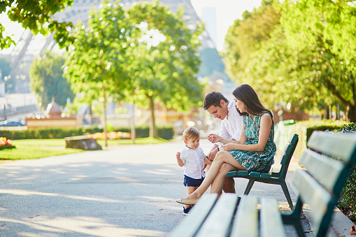 Happy family of three sitting on the bench in park near the Eiffel tower and enjoying their vacation in Paris, France