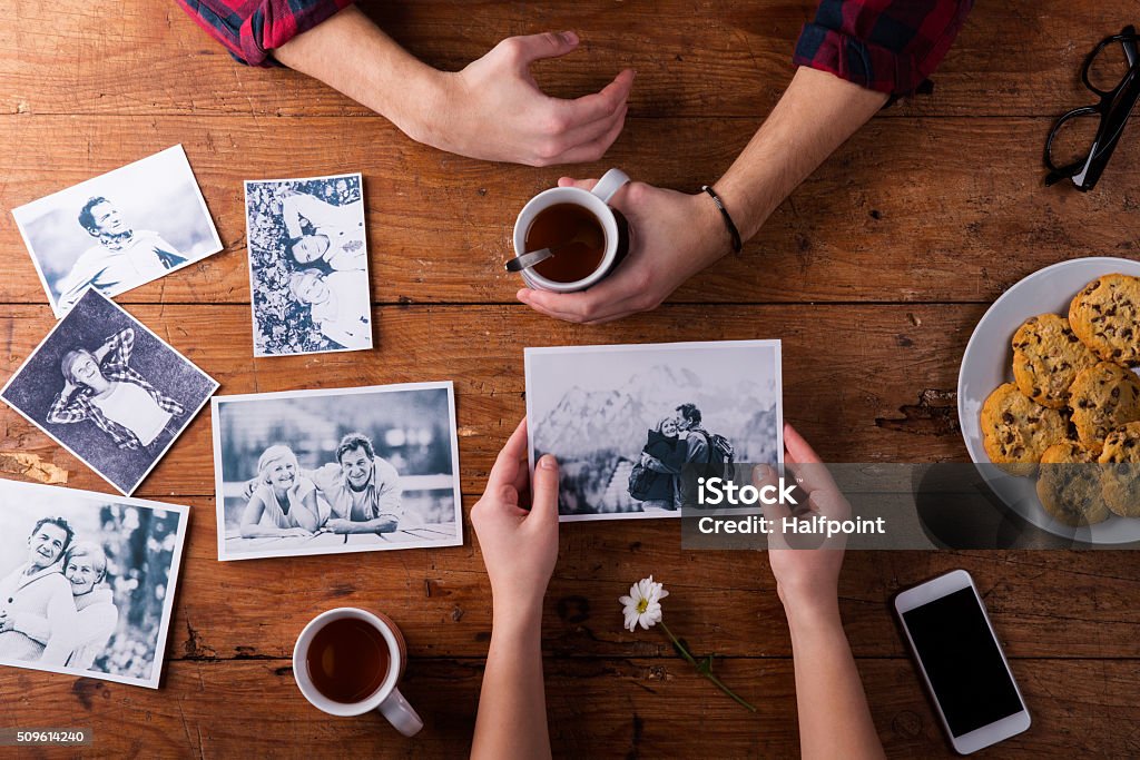 Mans and womans hands. Black-and-white photos. Couple. Tea, cook Unrecognizable mans and womans hand. Looking  at their black and white photos. Couple in love. Cookies and tea, daisy flower, smart phone. Valentines day composition. Studio shot on brown wooden background. Looking Stock Photo