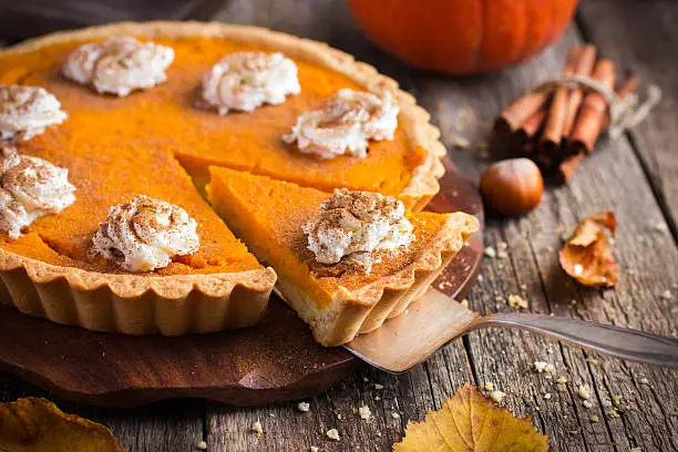 pumpkin pie with whipped cream and cinnamon on rustic background, top view