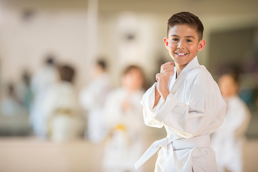 A multi-ethnic group of elementary age children are standing together in formation during their karate class. One boy is smiling while looking at the camera.