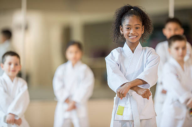Beginning a Karate Class A multi-ethnic group of elementary age children are standing together in formation during their taekwando class. One girl is smiling while looking at the camera. martial arts photos stock pictures, royalty-free photos & images
