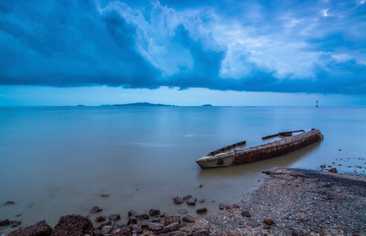 A boat wreckage stranded near a muddy seashore before the storm arrive. 