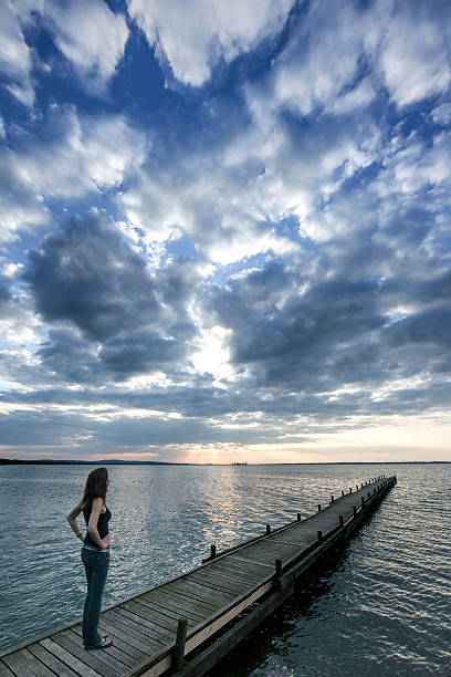 istock Woman on lakeside jetty watching majestic sunset cloudscape 509624956