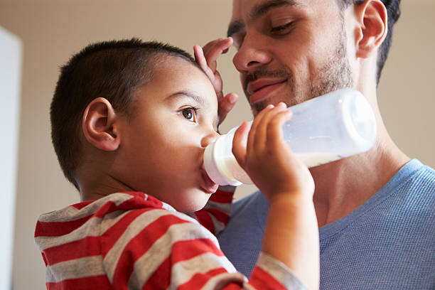 istock Father Carrying Young Son As He Drinks Milk From Bottle 509625582