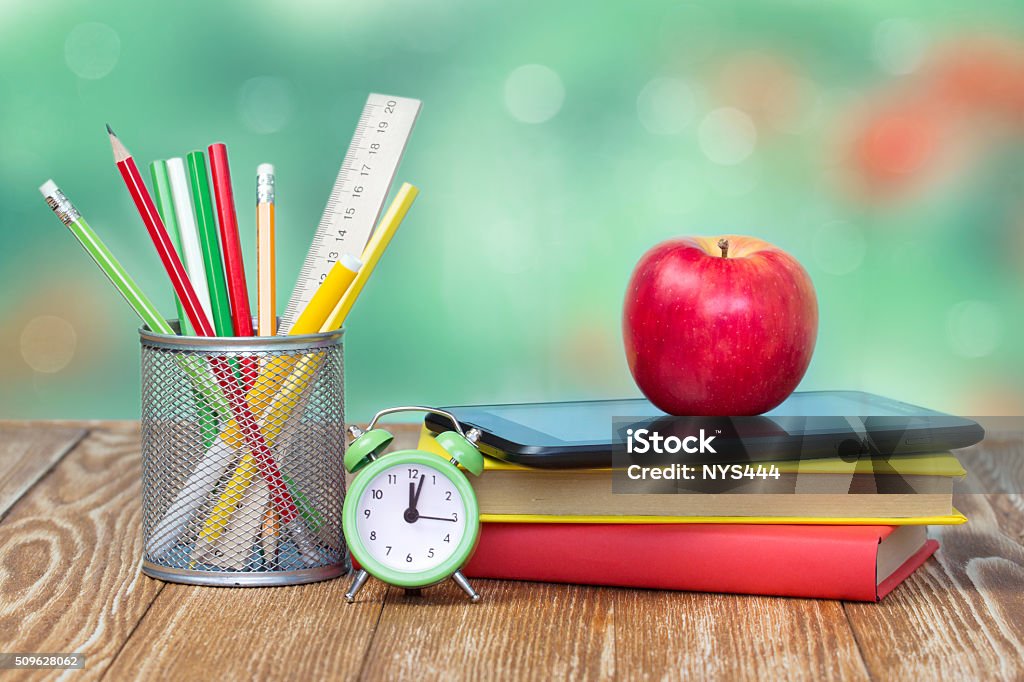 School supplies on green empty space background. School supplies on wooden table desk nature green background empty space.Apple stack books stationary alarm back to school concept. Apple - Fruit Stock Photo