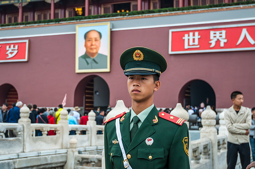 Beijing, China - October 13, 2013: A Chinese soldier stands guard in front of the Gate of Heavenly Peace between Tiananmen Square and The Forbidden City in Beijing, China. Behind the soldier is a large portrait of Chairman Mao Zedong, leader of the Communist Party of China.