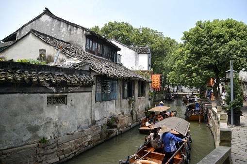 Tongli, China - July 19, 2015: Boats carrying tourists on the canals of historic Tongli, a popular water town in Wujiang county, on the outskirts of Suzhou. It is known for a system of canals, and its many bridges. The place retains many of the features of an ancient Wu region town.