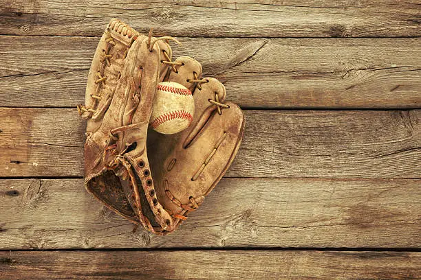 Vintage baseball mitt and ball on grungy, rough wood background viewed from above