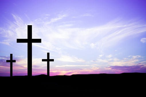 Easter.  The crucifixion.  Three wooden crosses in silhouette stand silently on a hill at sunset.  The dramatic sky is beautiful in its pink and purple colors.  Christianity, religious themes. Copyspace.