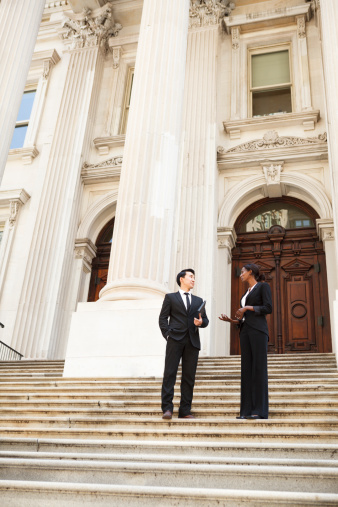 A well dressed man and woman in conversation on steps of a legal or municipal building. Could be business or legal professionals or lawyer and client.