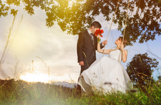 groom smelling flowers and bride on swing.