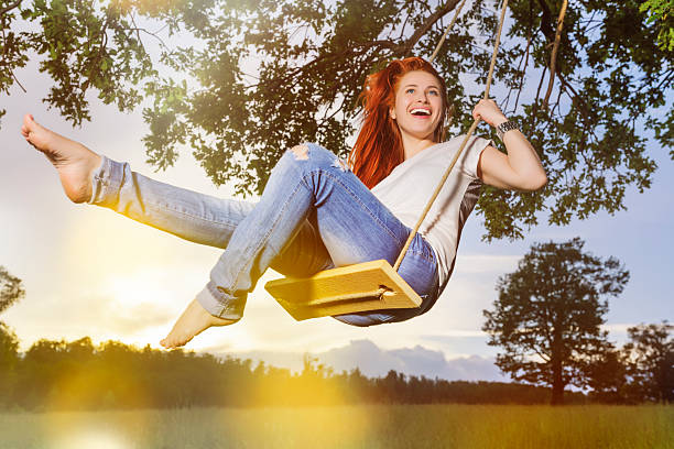 Crazy woman play and have fun on a swing flying high with trees and sky in background. Happy female people enjoy outdoor leisure activity and playful lifestyle
