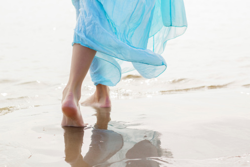 Woman with blue skirt walking on the beach on hot summer day.